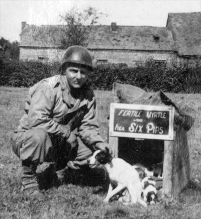Photo of Pfc "Benny" Benevento, 14th Chemical Maintenance Company, US Army, and company mascot dog "Fertile Myrtle" and her six puppies taken near La Capelle, France, mid-September 1944.