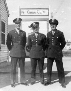 Photo of 1st Lt Arthur Schoenewaldt, 1st Lt Robert Marmorstein, 2nd Lt Walter Kovacs of 14th Chemcial Maintenance Company standing in front of company crest in their WW-II U.S. Army uniforms, at Camp Gordon, Georgia, circa October-November 1943