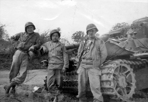 Photo of T/Sgt John Bogden, T/5 Harold A. Andrews, and Pfc William Long of 14th Chemical Maintenance Company, in their WW-II U.S. Army uniforms posing next to a wrecked German Panzer IV Type H tank, taken circa 05 August 1944 near St. Lo, France